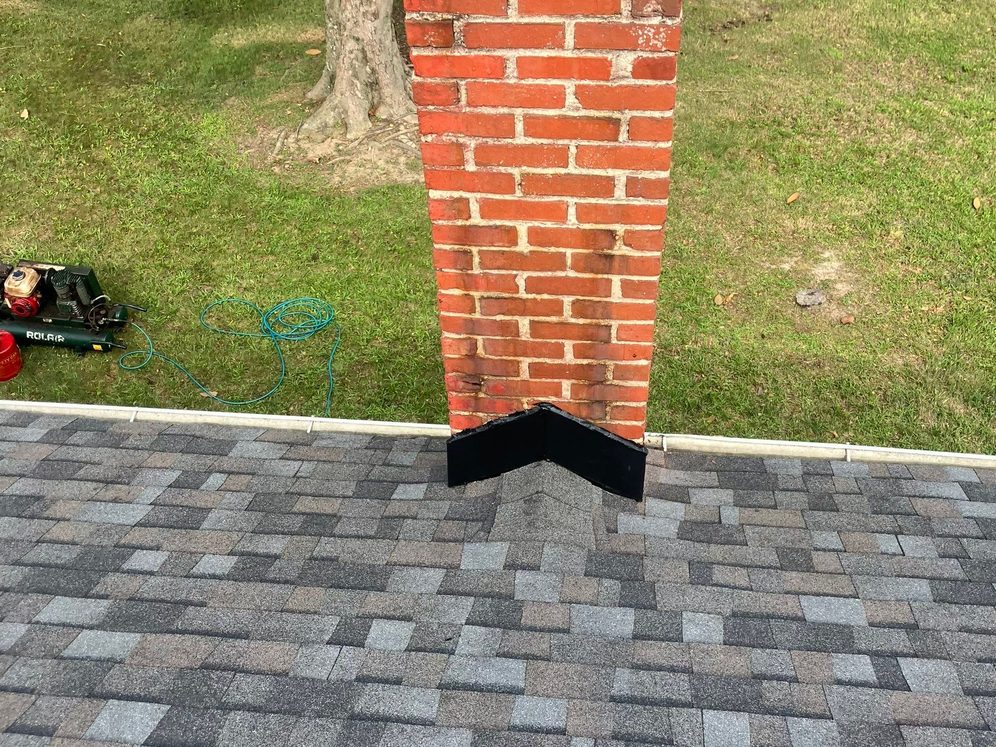 The same red brick chimney on the finished gray architectural shingle roof, with new black base flashing worked in around it