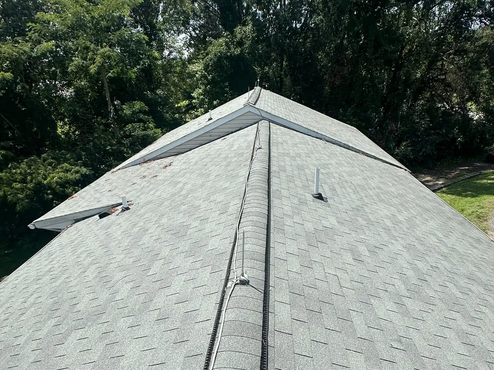 Looking along a ridge of old green-gray three-tab shingles toward a gable end with white roof vents