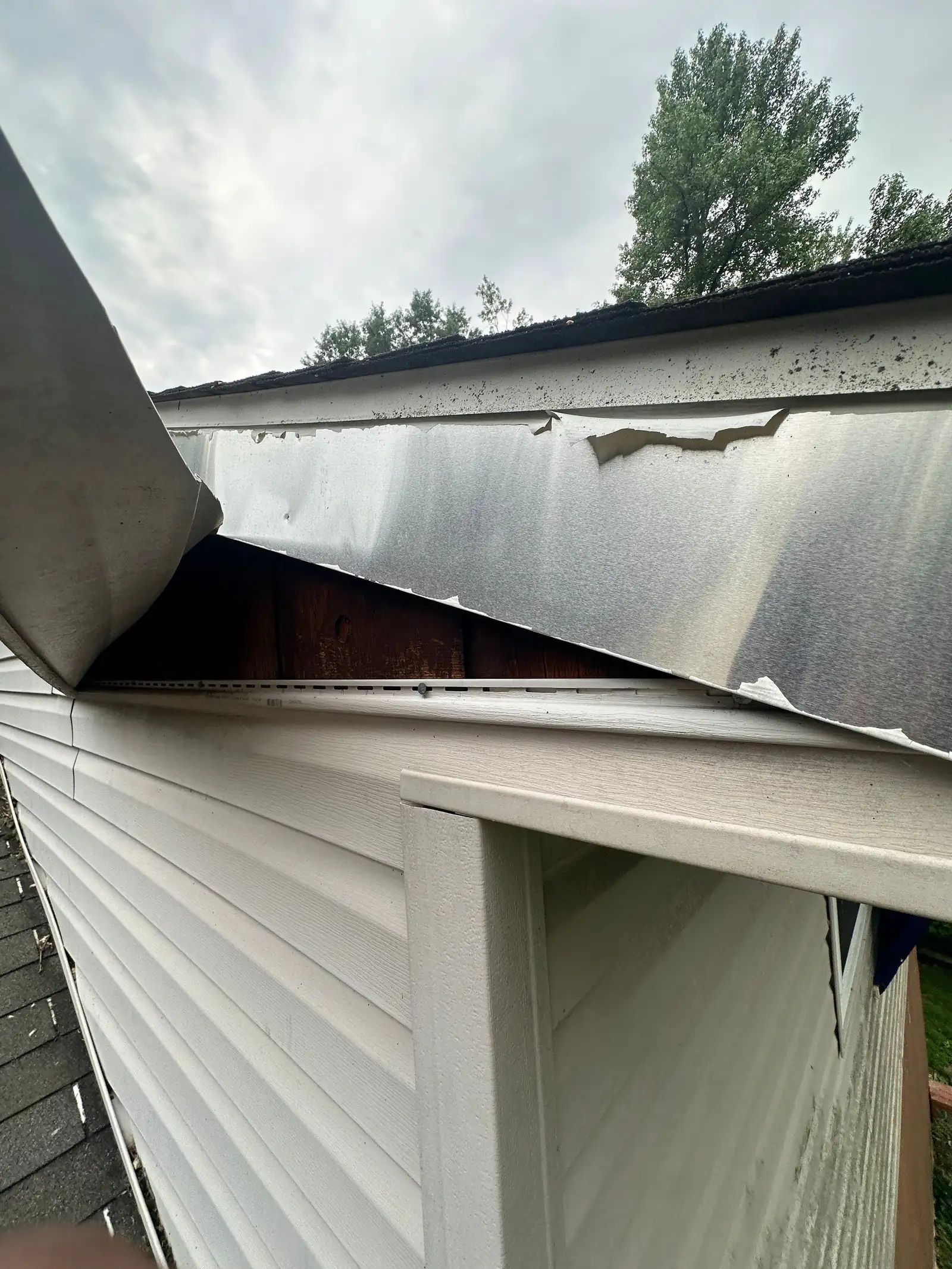 Displaced metal at the roof edge exposing timber above white siding, photographed during the Columbia inspection