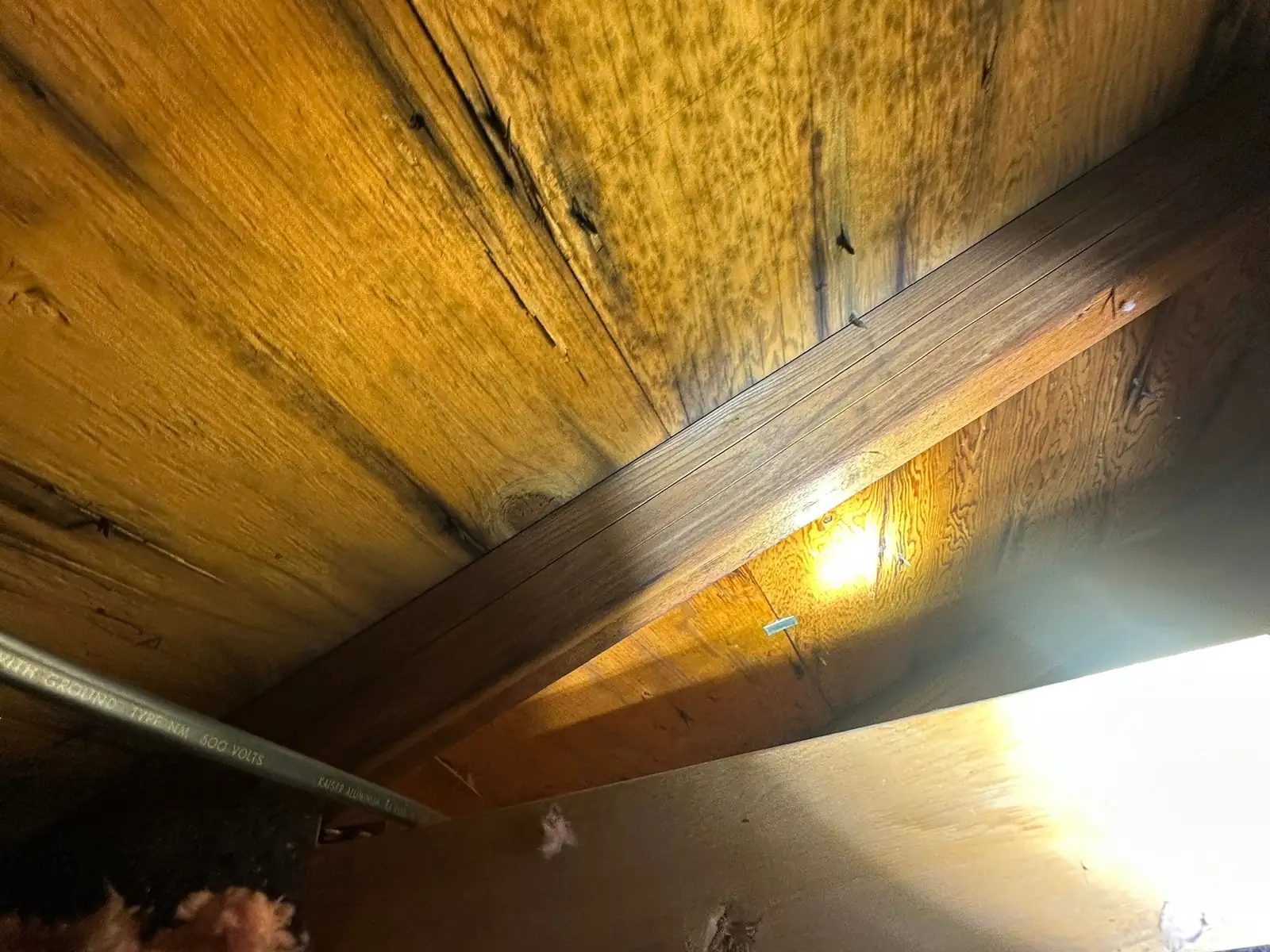 Exposed roof decking and timber rafters above pink insulation, photographed through a ceiling opening