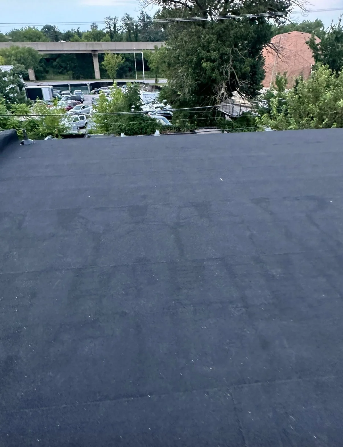 The same roof finished in smooth dark membrane, looking out over the same elevated highway and parking lot