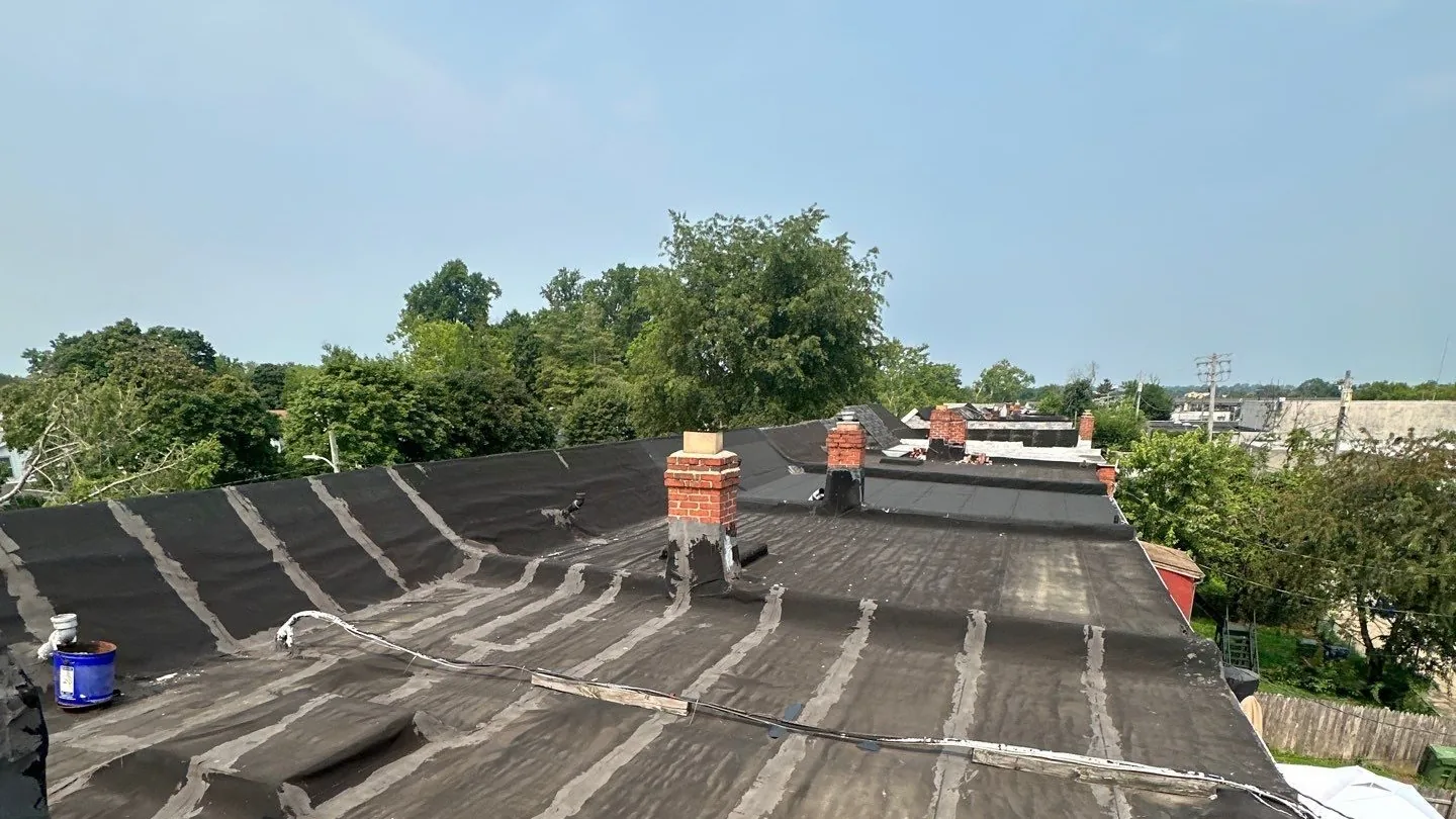 Long aged low-slope roof over a row of attached buildings, every seam in the old rolled roofing coated over