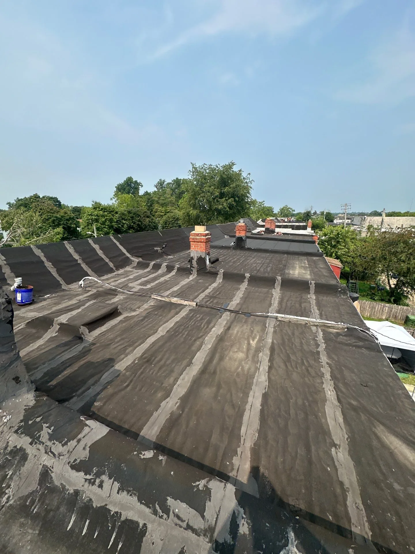 Long aged low-slope roof over a row of attached buildings, every seam in the old rolled roofing coated over