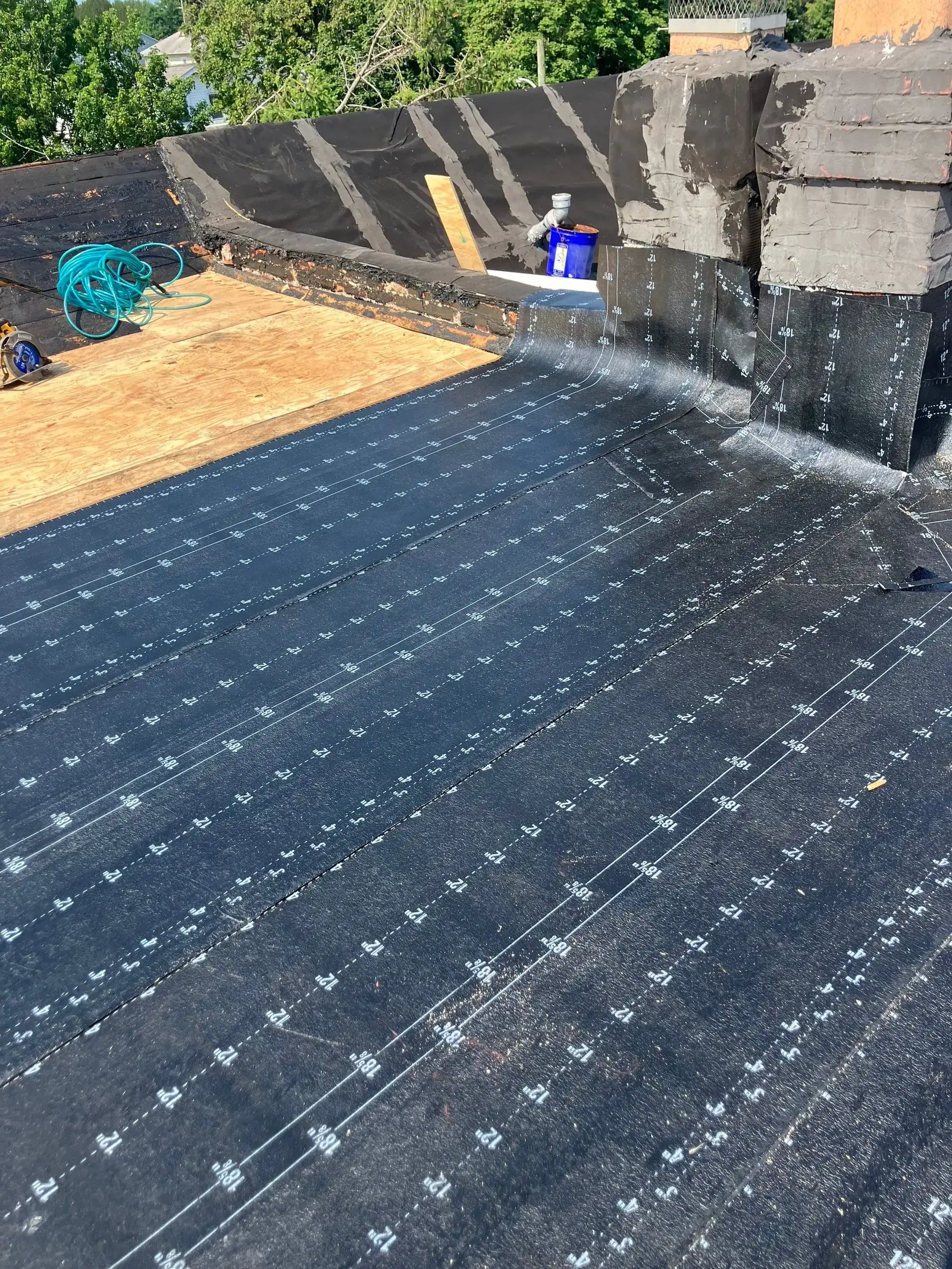 Modified bitumen base sheet with its printed fastener grid rolled across a low-slope roof deck, a chimney and parapet at the far end