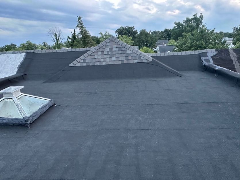 Finished low-slope roof in smooth black modified bitumen, with a shingled gable dormer and a skylight cupola at the left