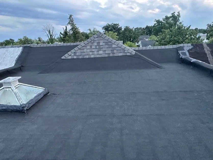 Finished low-slope roof in smooth black modified bitumen, with a shingled gable dormer and a skylight cupola at the left