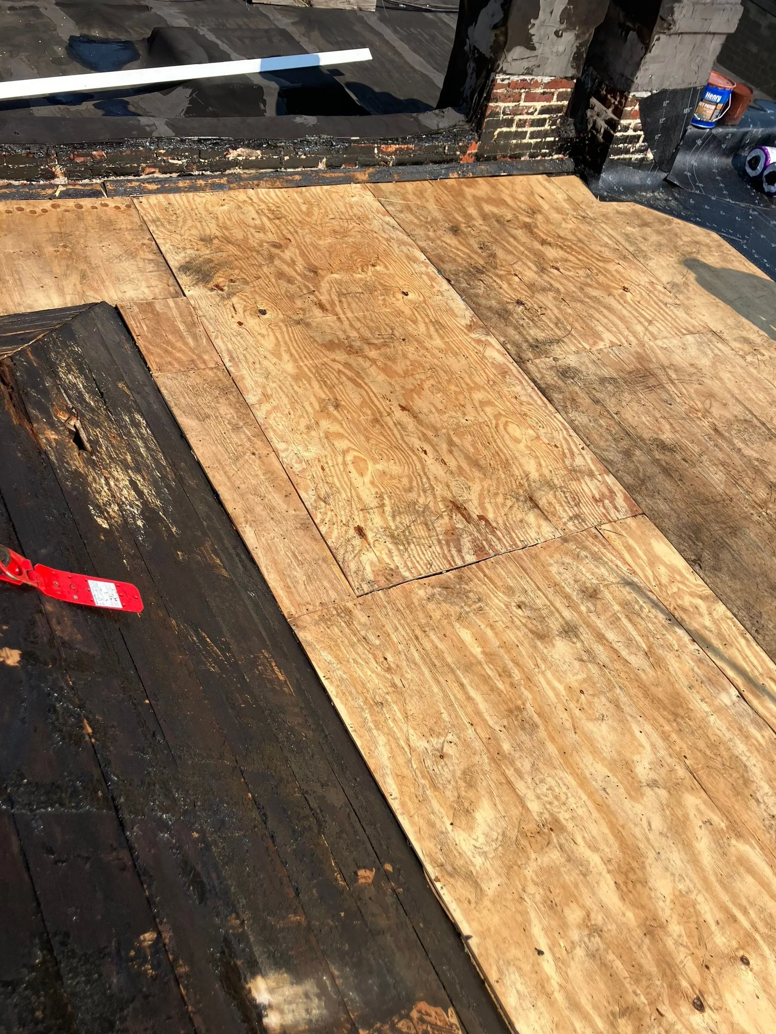 New plywood sheathing fastened over the old plank decking of a low-slope roof, a red tape measure lying on the sheet