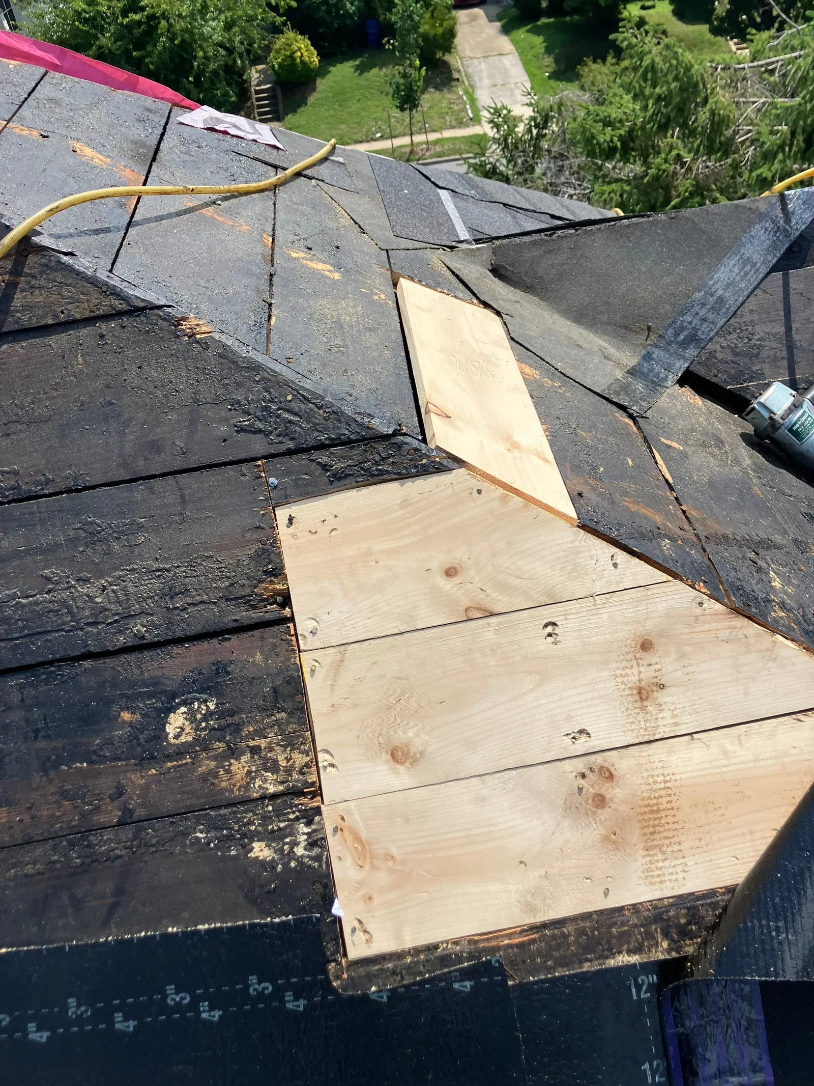 A sheet of new plywood let into the old plank decking of a low-slope roof, a yellow air hose running across the black underlayment