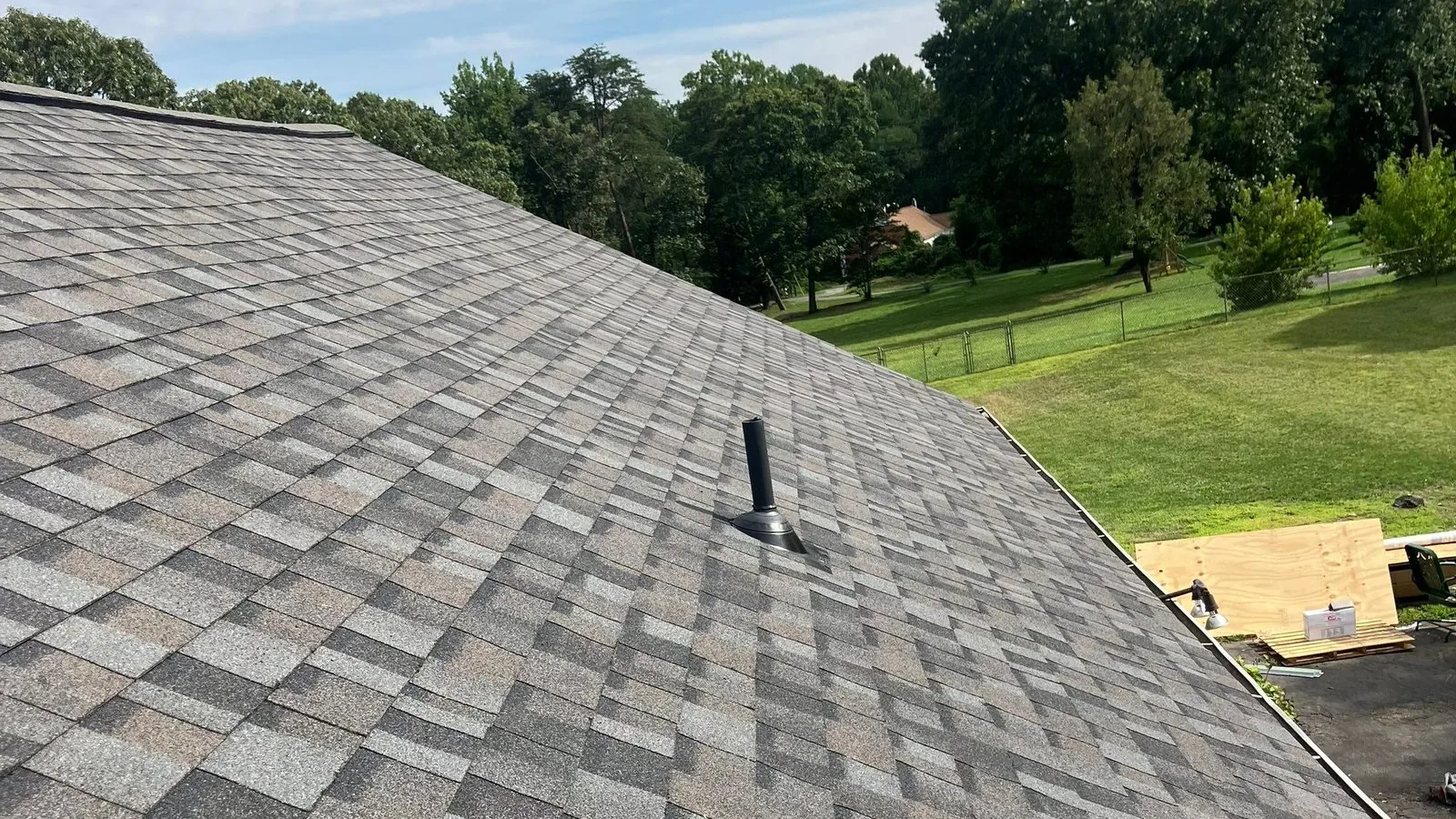 New gray architectural shingle roof with a black plumbing vent boot set into the field, lawn and trees beyond