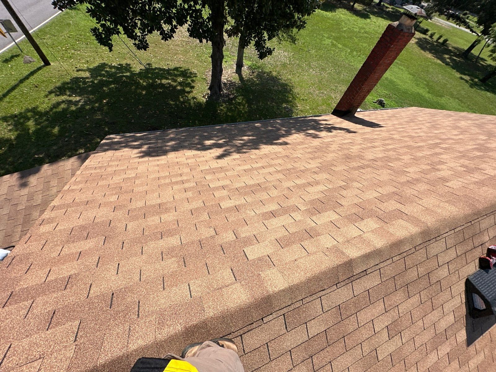 Across the aging tan three-tab hip roof toward the brick chimney and the open lawn