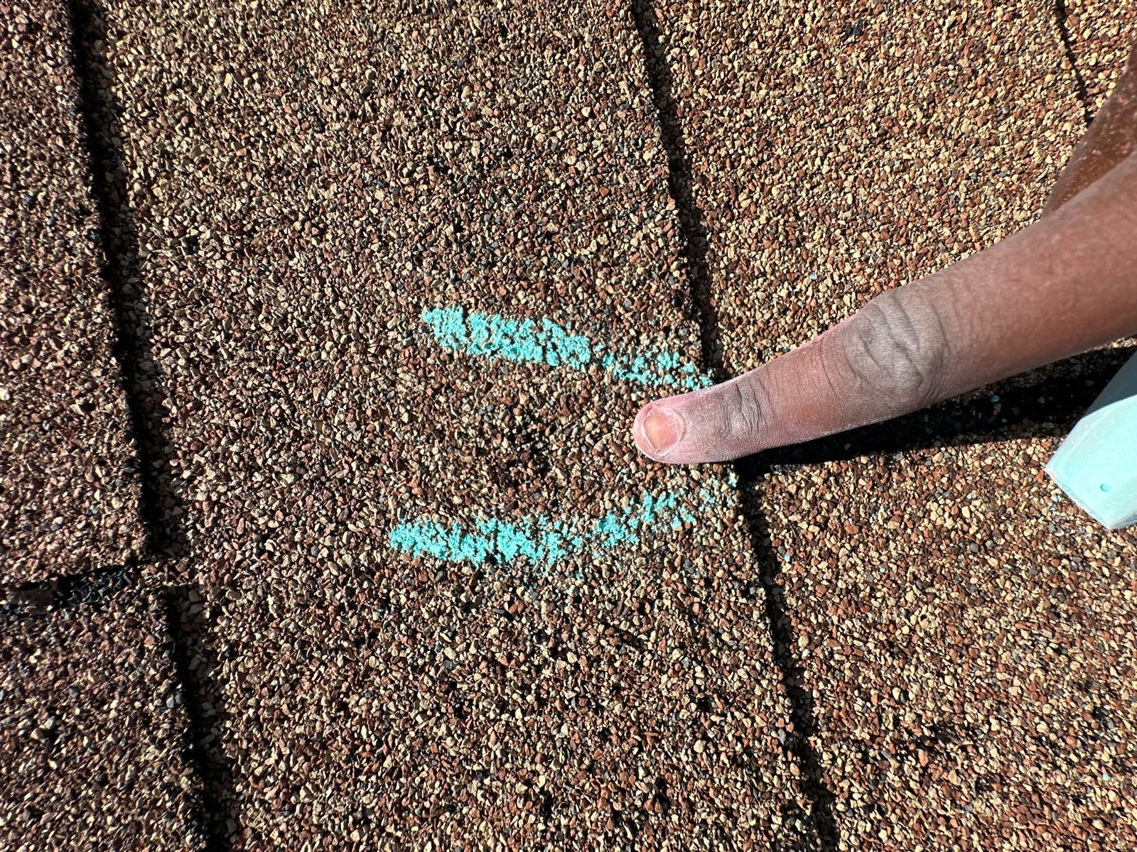 Two chalk marks on a tan three-tab shingle with the inspector's chalk stick alongside