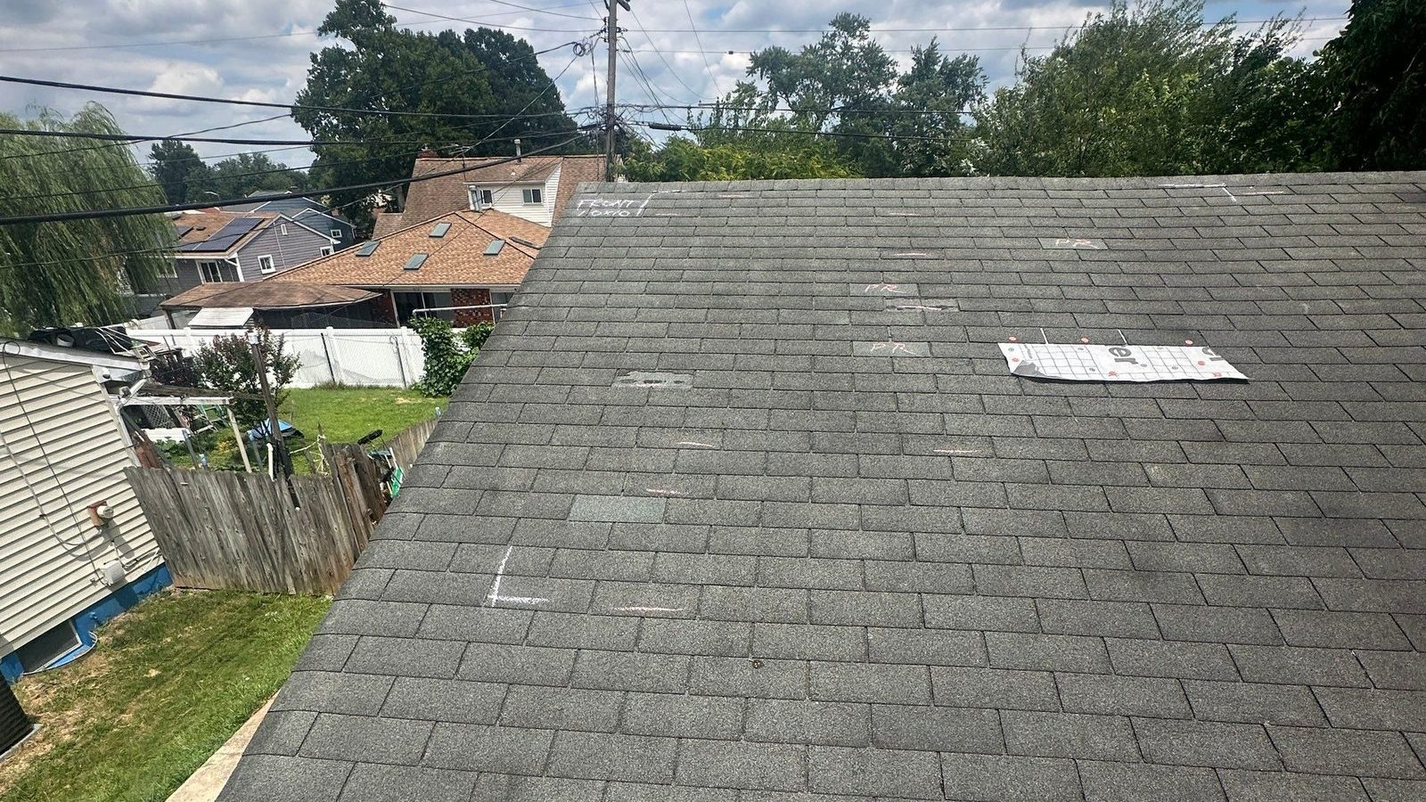 Aged gray three-tab shingle slope shot toward the eave, with white and pink chalk marks ringing damaged shingles