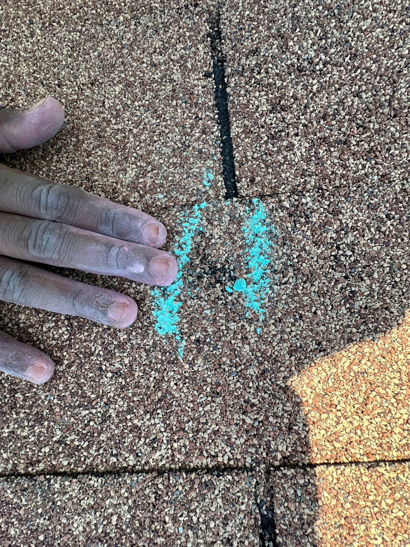 Chalk circle drawn around an impact bruise on a weathered three-tab asphalt shingle, an inspector's hand beside it