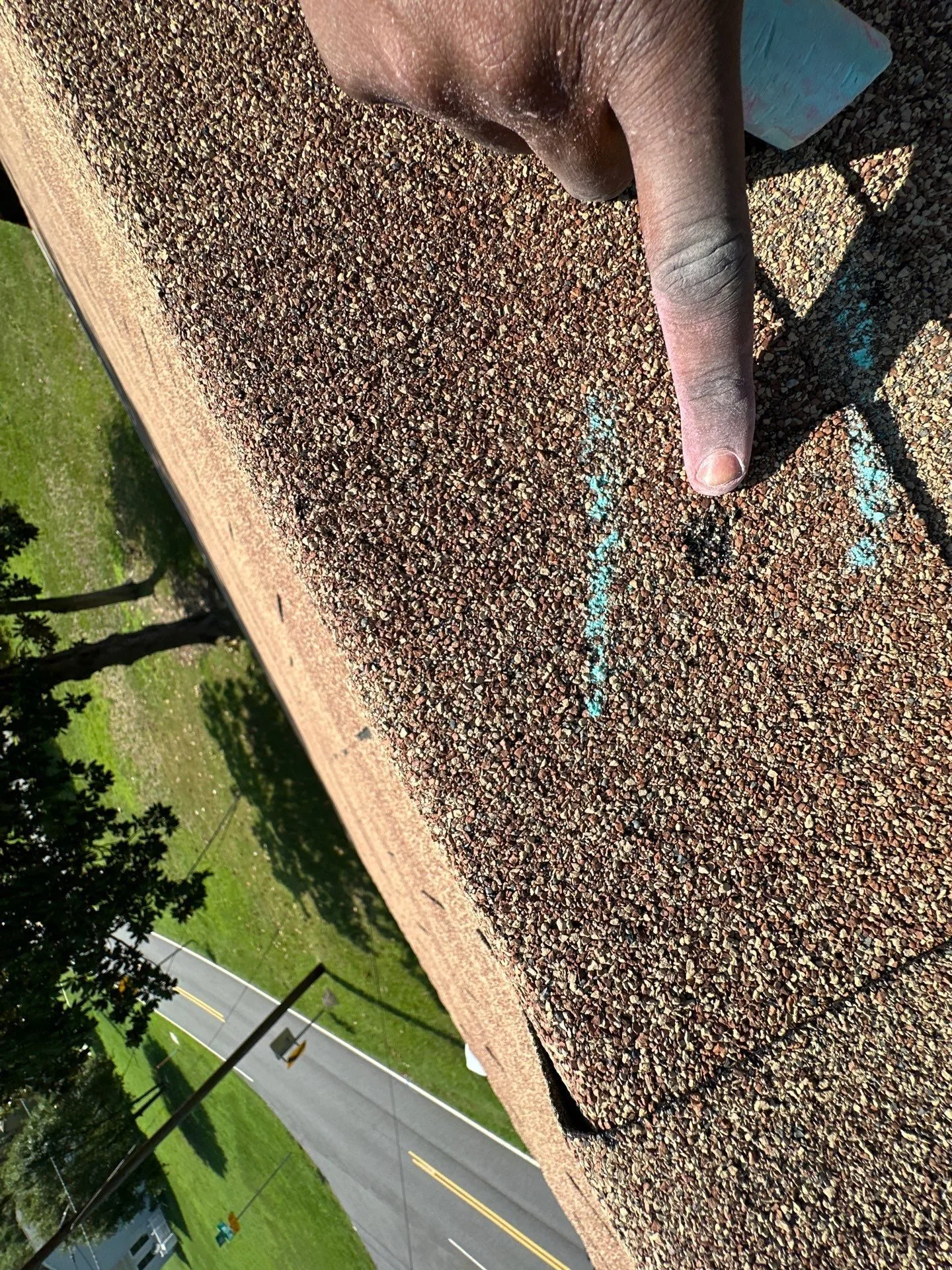 Looking down the eave edge of a tan shingle roof at a chalk-marked hail hit