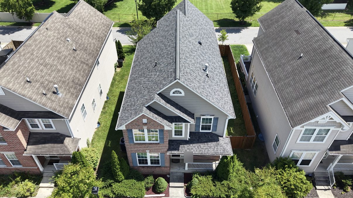 Aerial view of a finished gray architectural shingle roof on a two-storey brick and siding suburban home between two neighboring houses