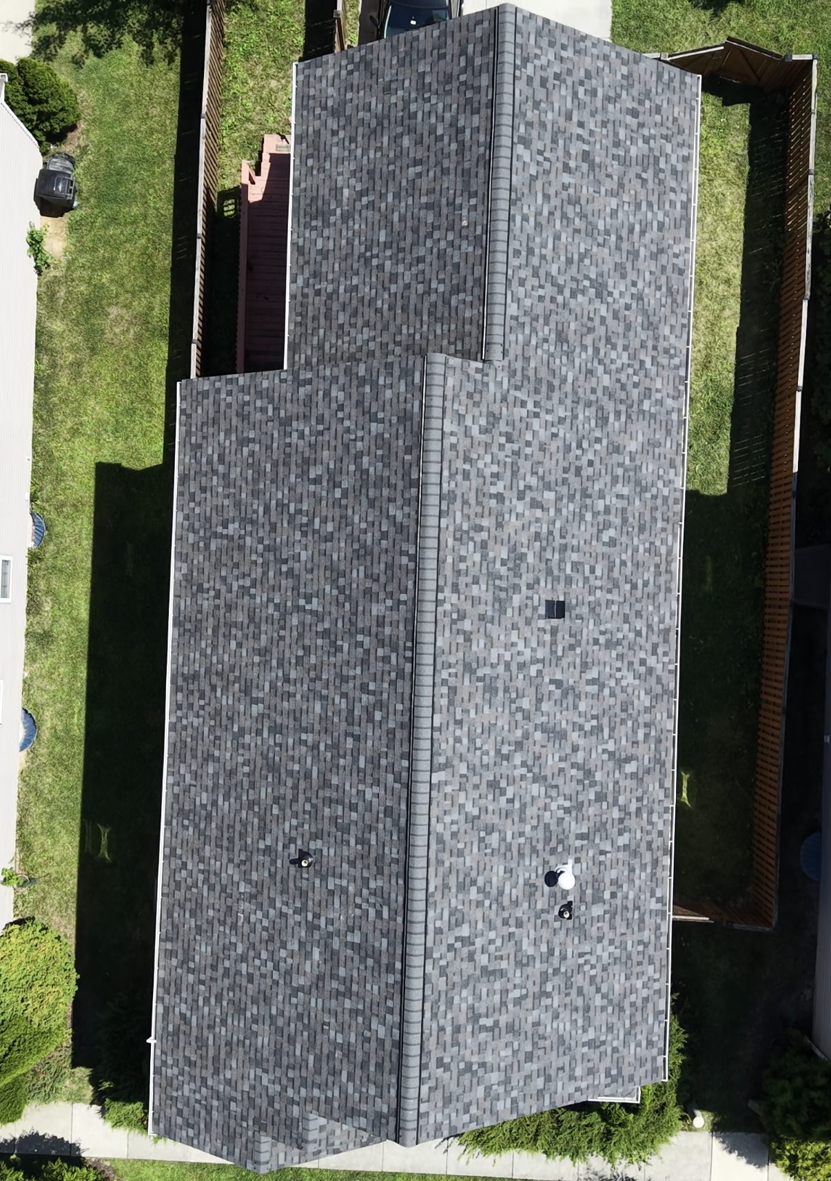 Overhead aerial of a finished gray shingle roof with several intersecting gable planes and ridge lines, pipe vents visible