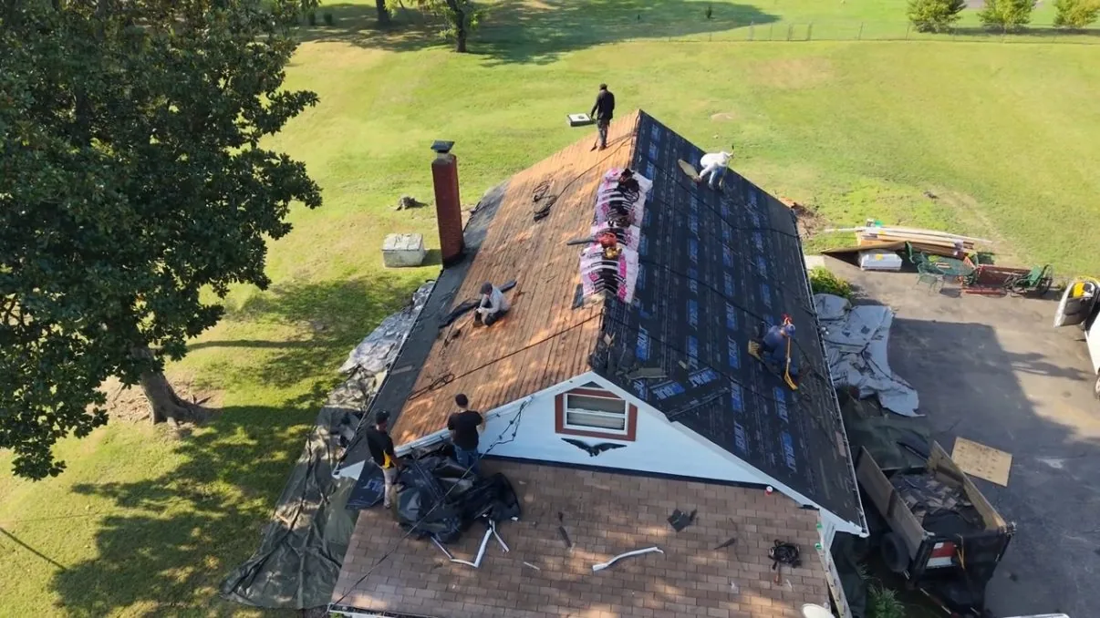 Aerial view down onto the same cottage mid tear-off, one slope stripped to its original wood plank decking