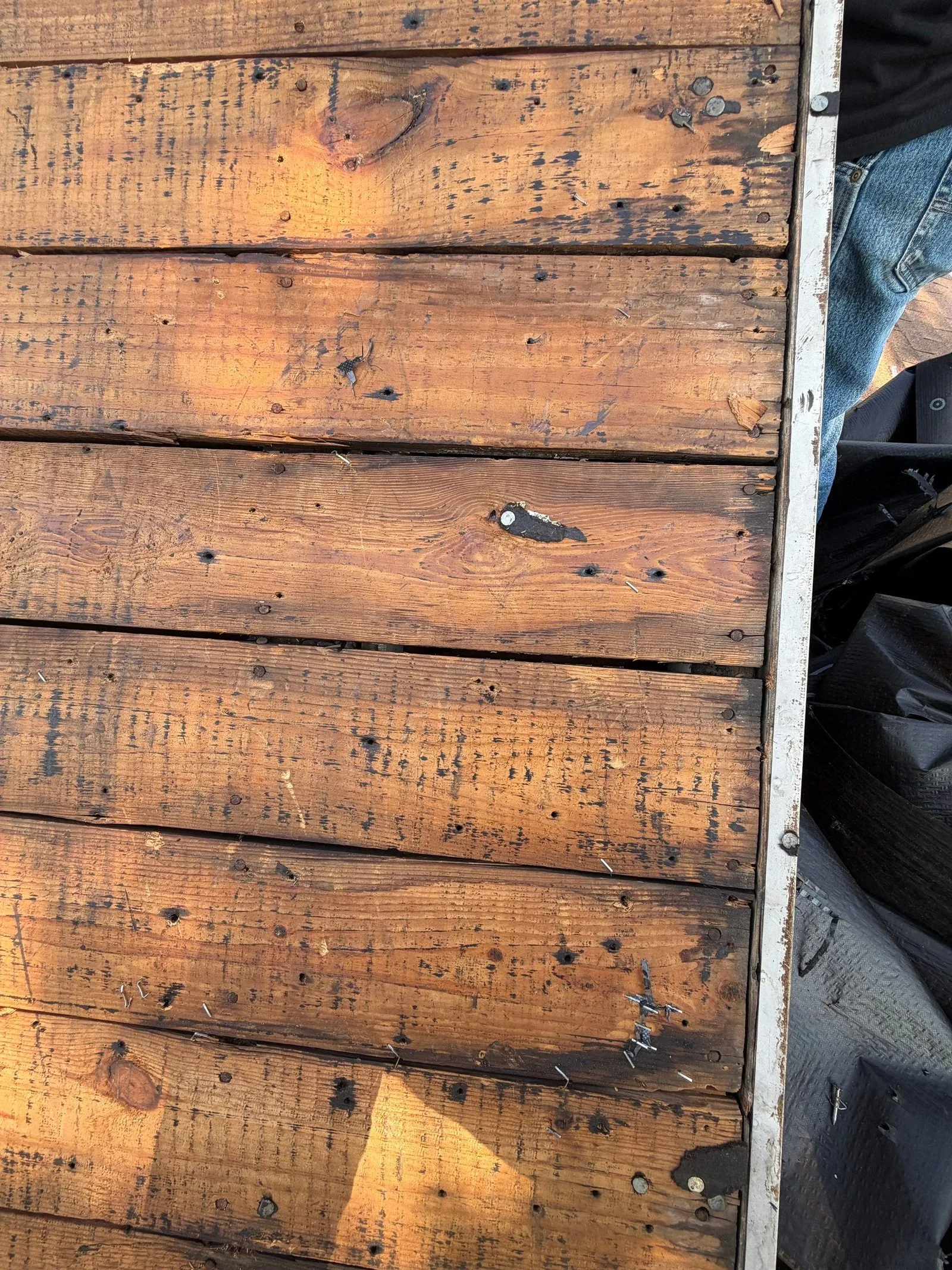 Bare wood plank roof decking exposed after the shingle tear-off, low sun raking across the boards