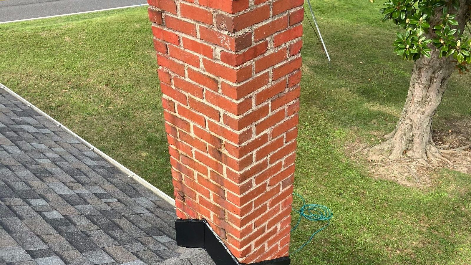 Red brick chimney on a finished gray architectural shingle roof with new black flashing at its base