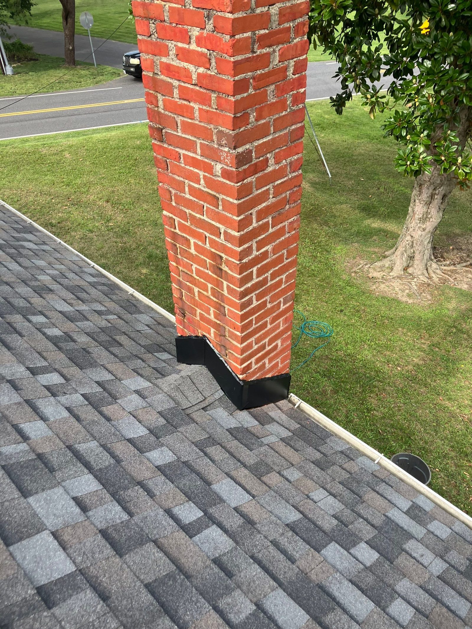 Red brick chimney on a finished gray architectural shingle roof with new black flashing at its base