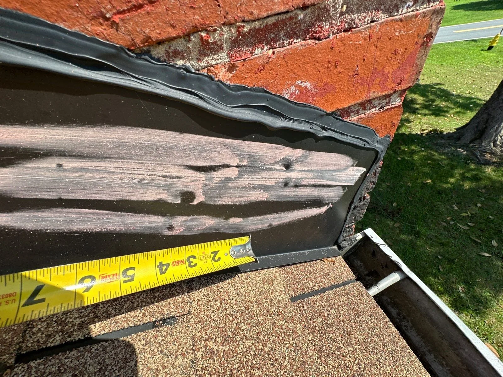 New black chimney flashing checked with a tape measure on the old tan shingle roof
