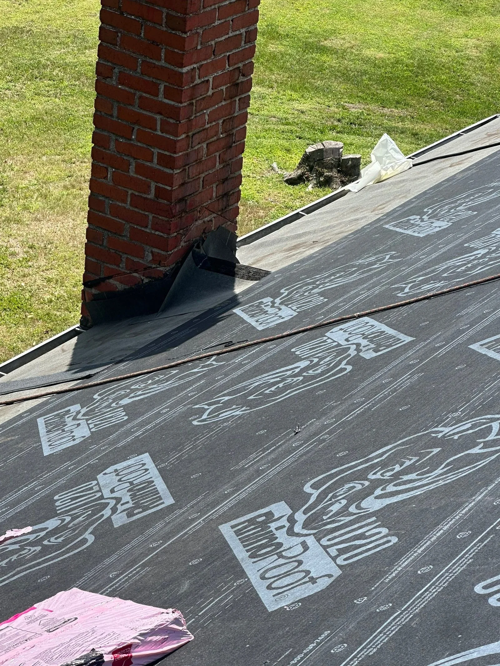 New black base and step flashing set in at the chimney on an underlayment-covered roof deck