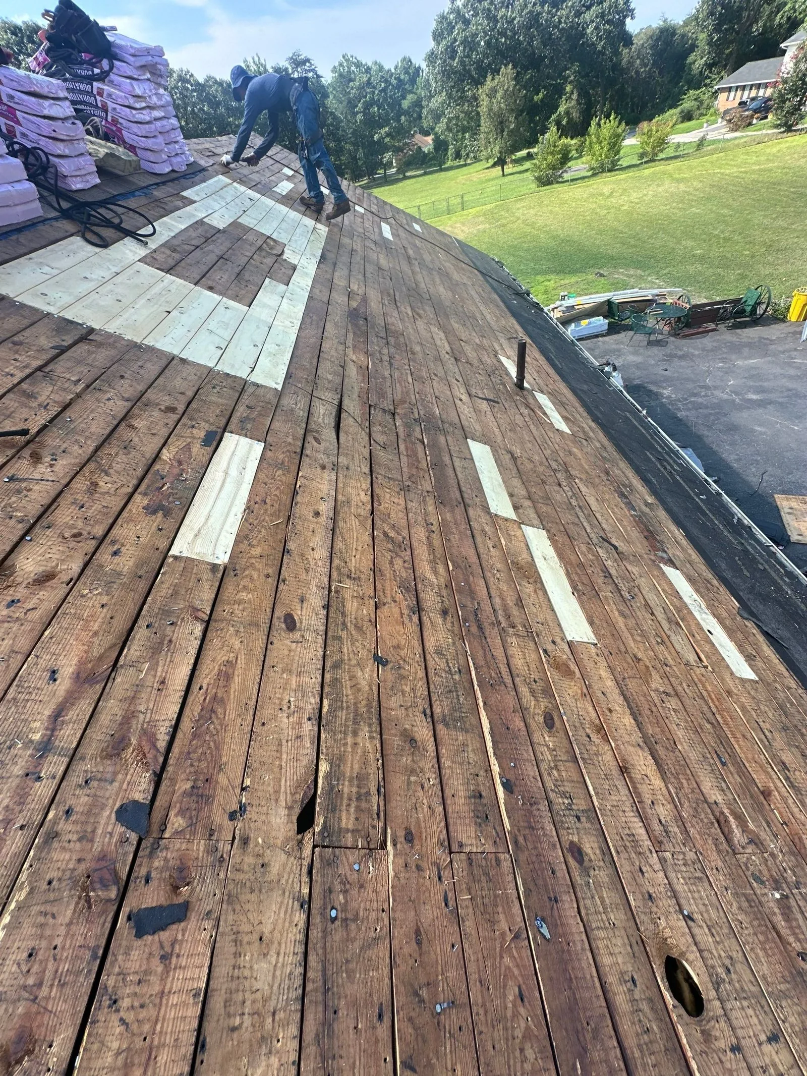 Roofer crouched on a stripped plank deck with new let-in boards and Owens Corning Duration bundles at the ridge