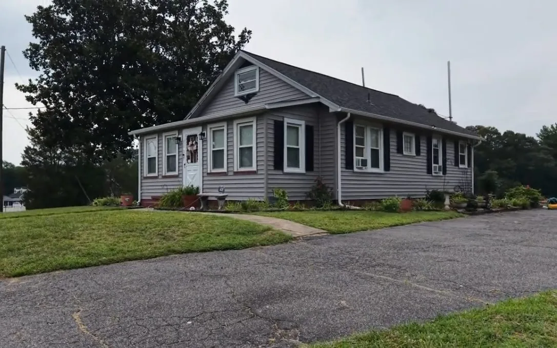 The finished cottage from the driveway under overcast light: gray lap siding, maroon window trim and a dark shingle roof