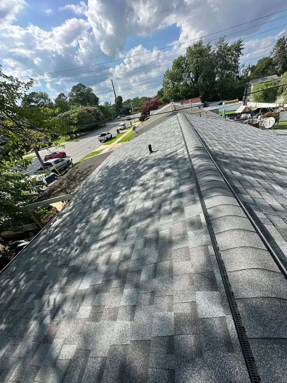 Finished gray shingle roof seen along the ridge, a continuous ridge vent running down the peak, street and homes visible below