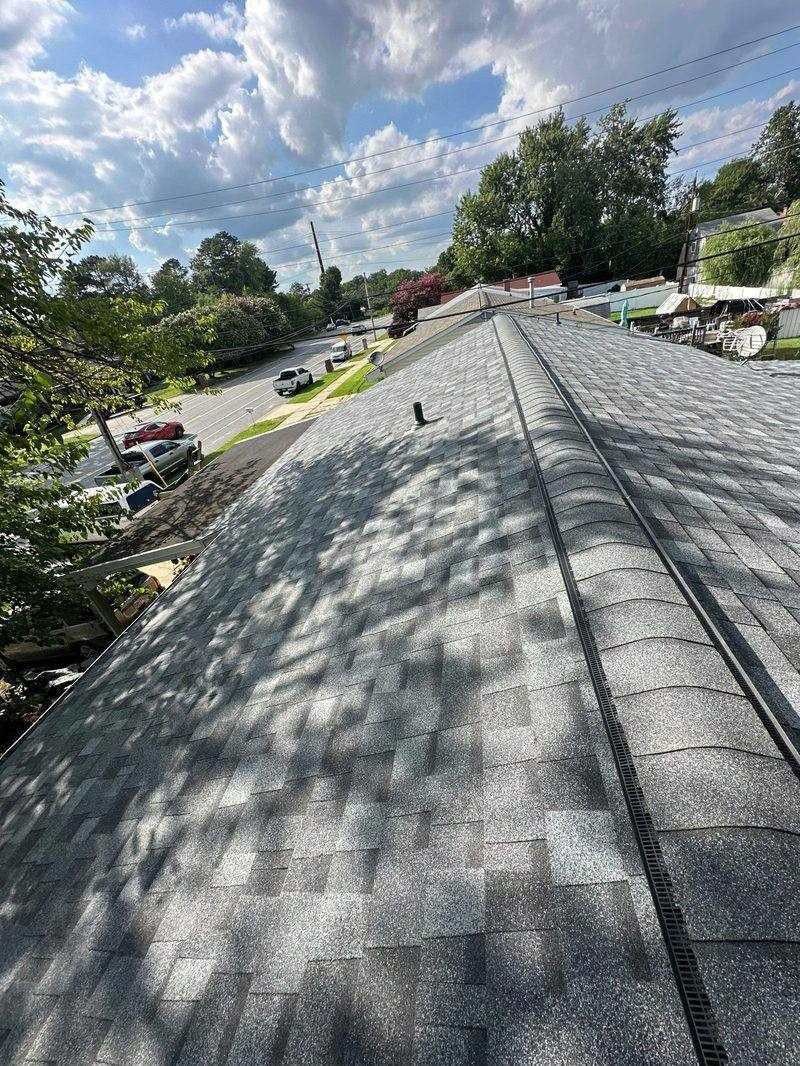 Finished gray shingle roof viewed along the ridge, a continuous ridge vent running down the peak, suburban street below