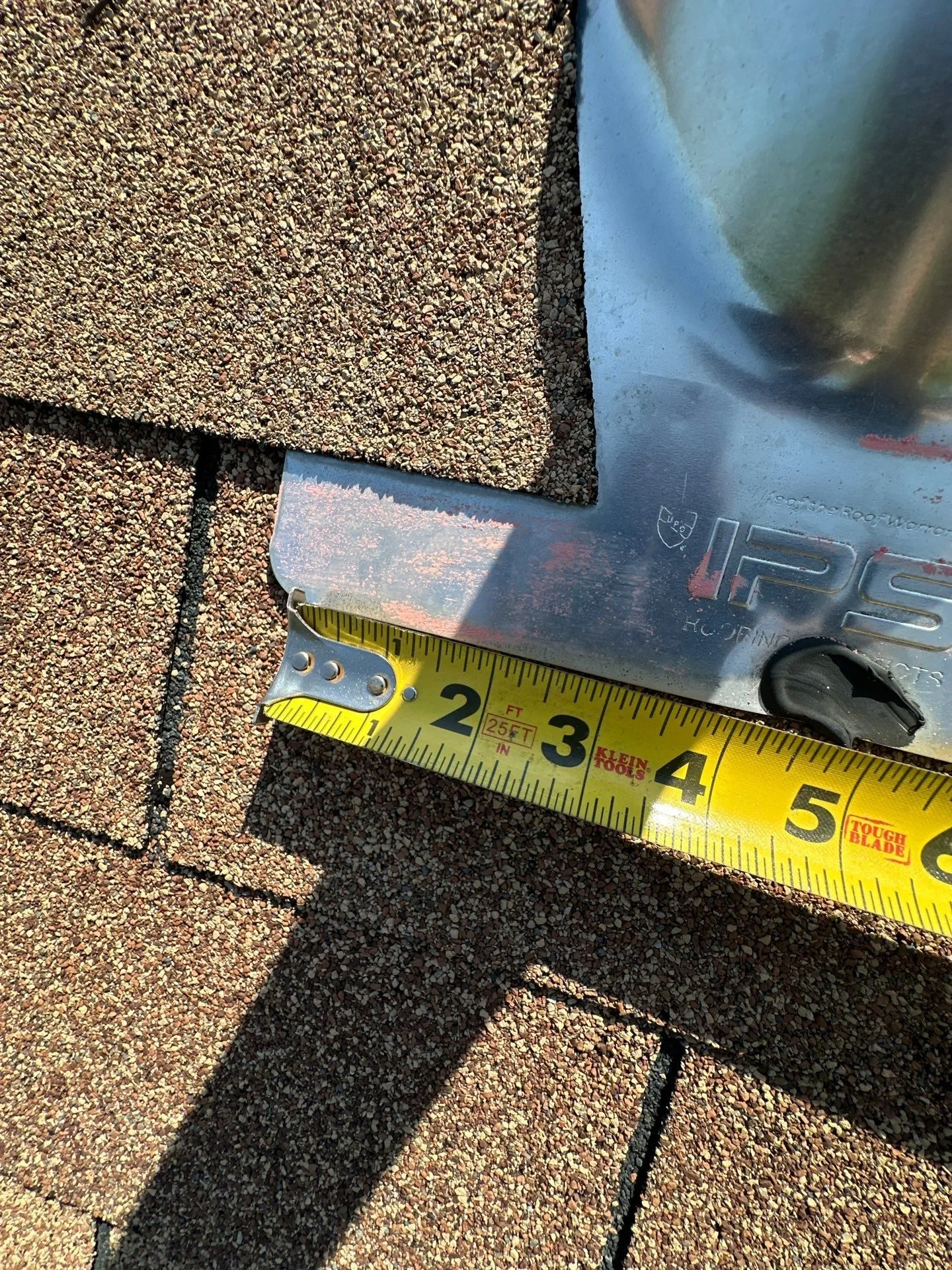 New metal pipe flashing installed in the shingle field with a tape measure laid across it
