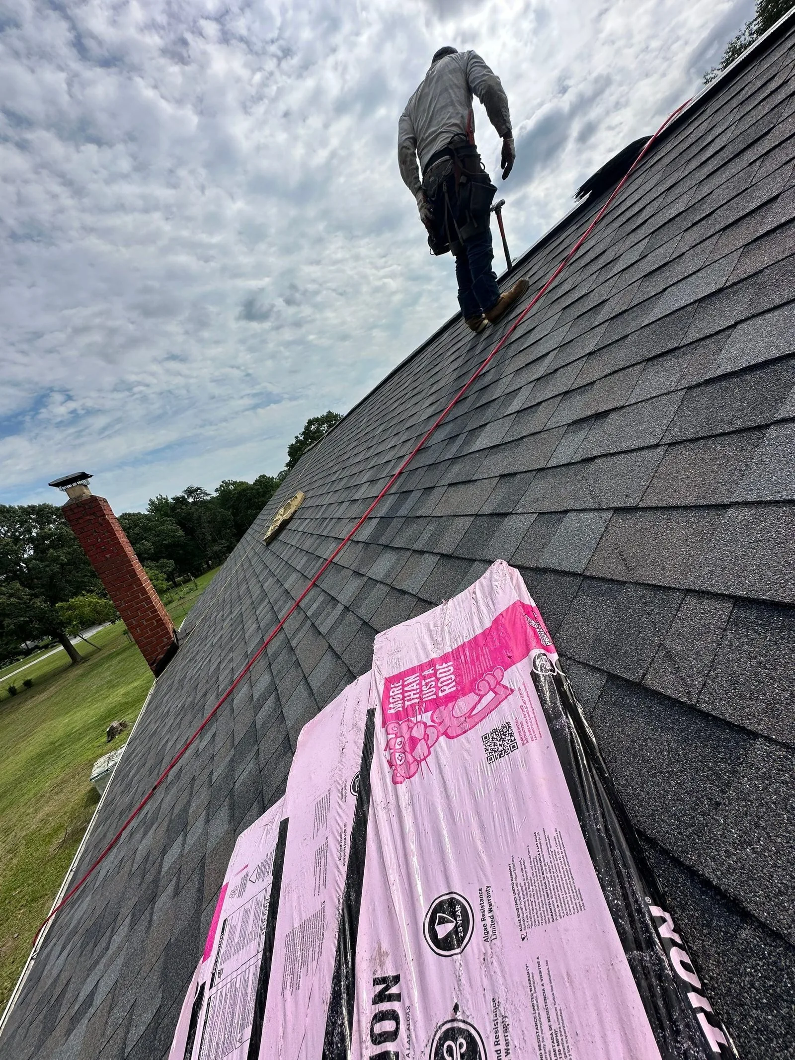 Roofer carrying a nail gun up the ridge during shingle installation