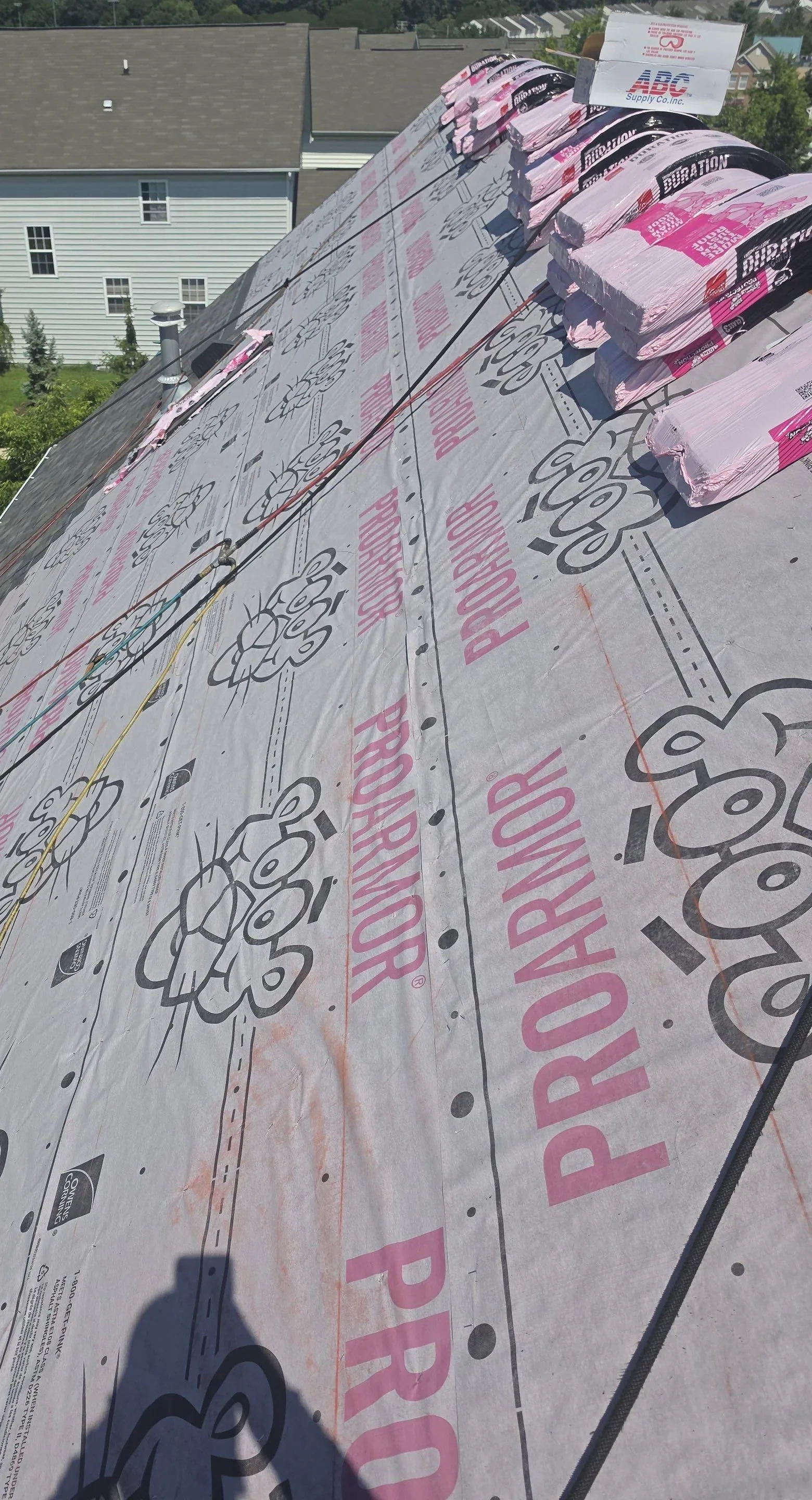 A whole steep slope covered edge to edge in printed synthetic underlayment, with Owens Corning Duration bundles at the ridge