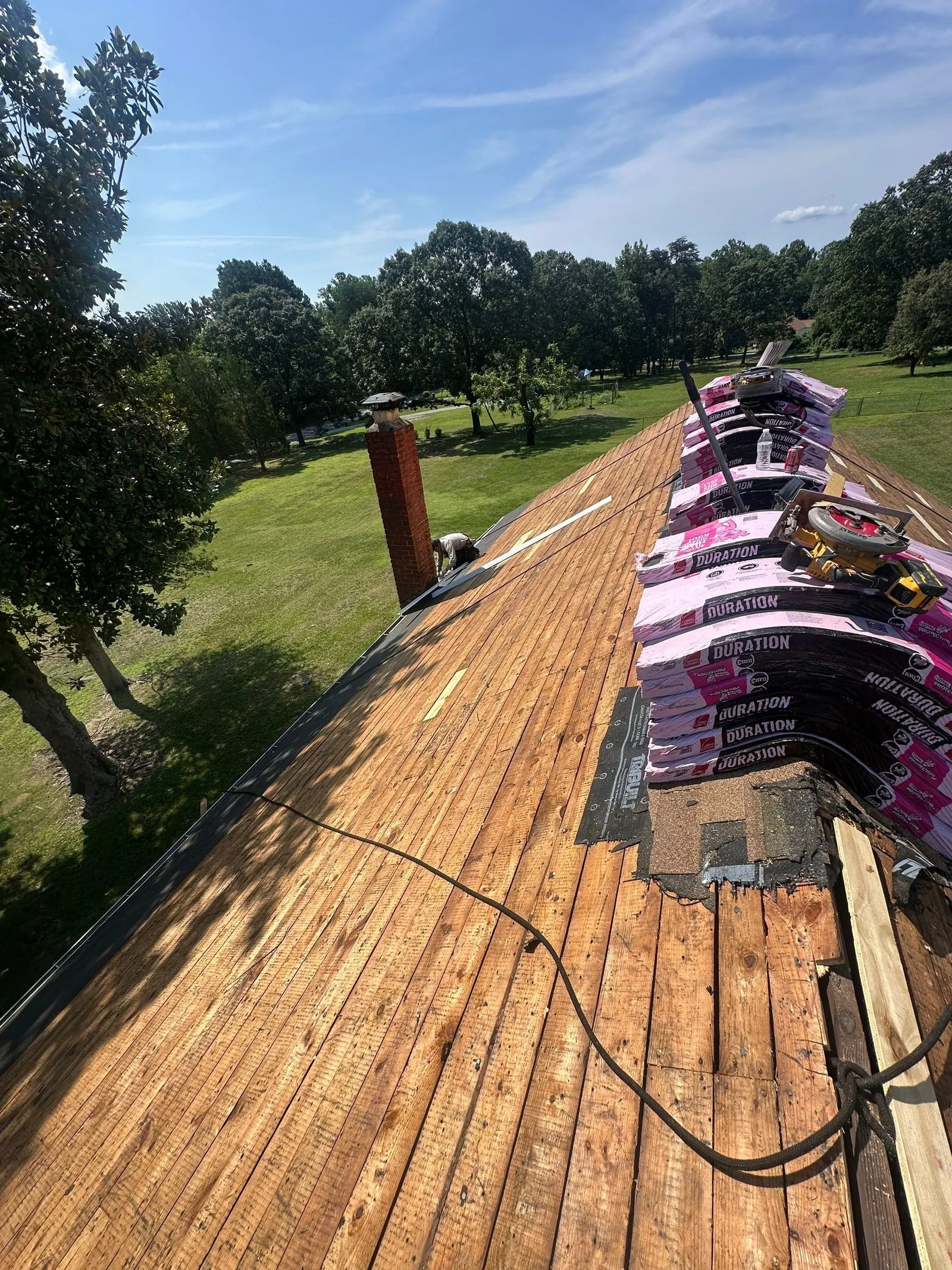 Stripped plank roof deck with Owens Corning Duration bundles along the ridge and a circular saw resting on them