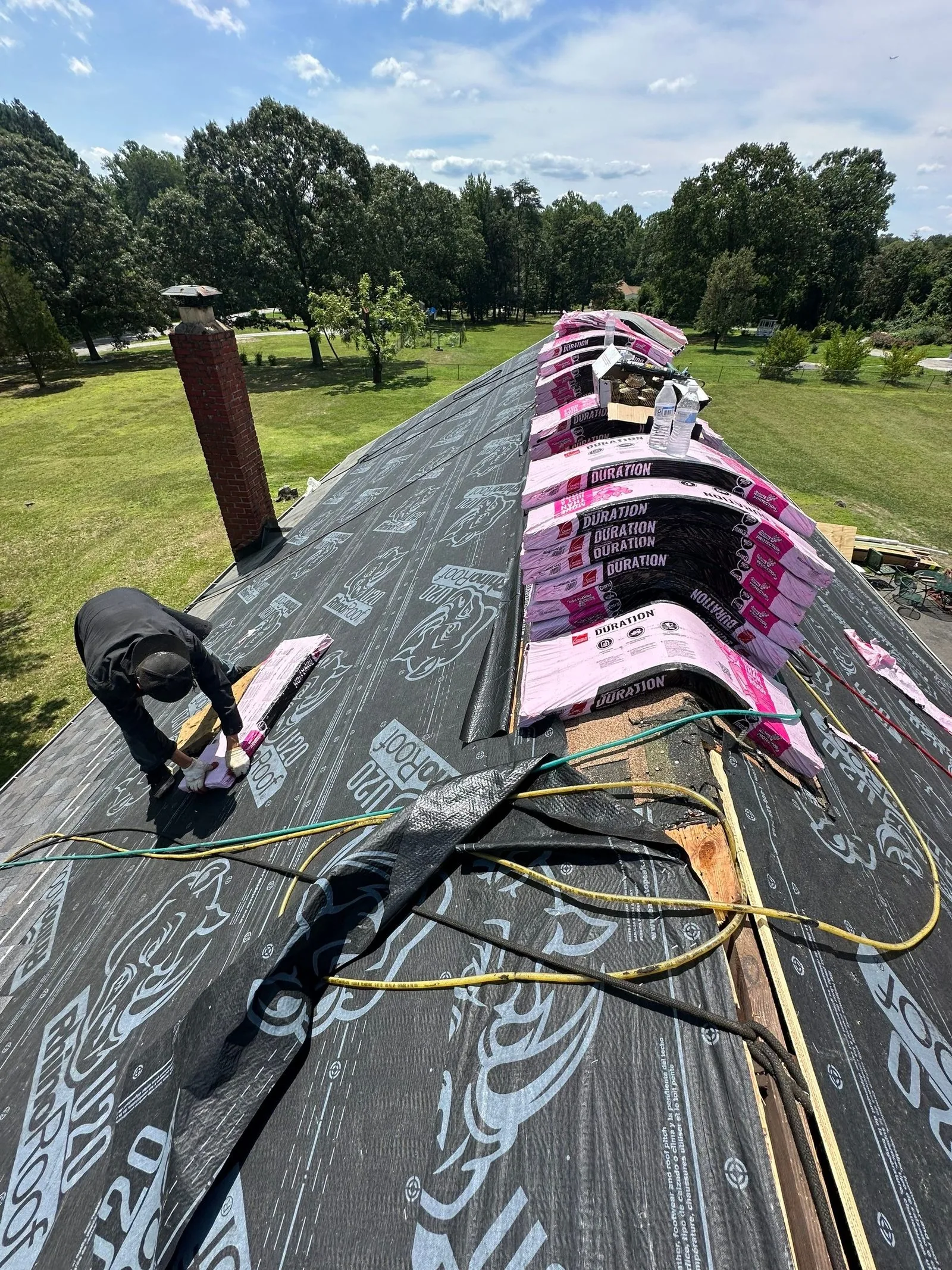 Roof deck covered in black printed synthetic underlayment, with wrapped shingle bundles along the ridge and an air hose