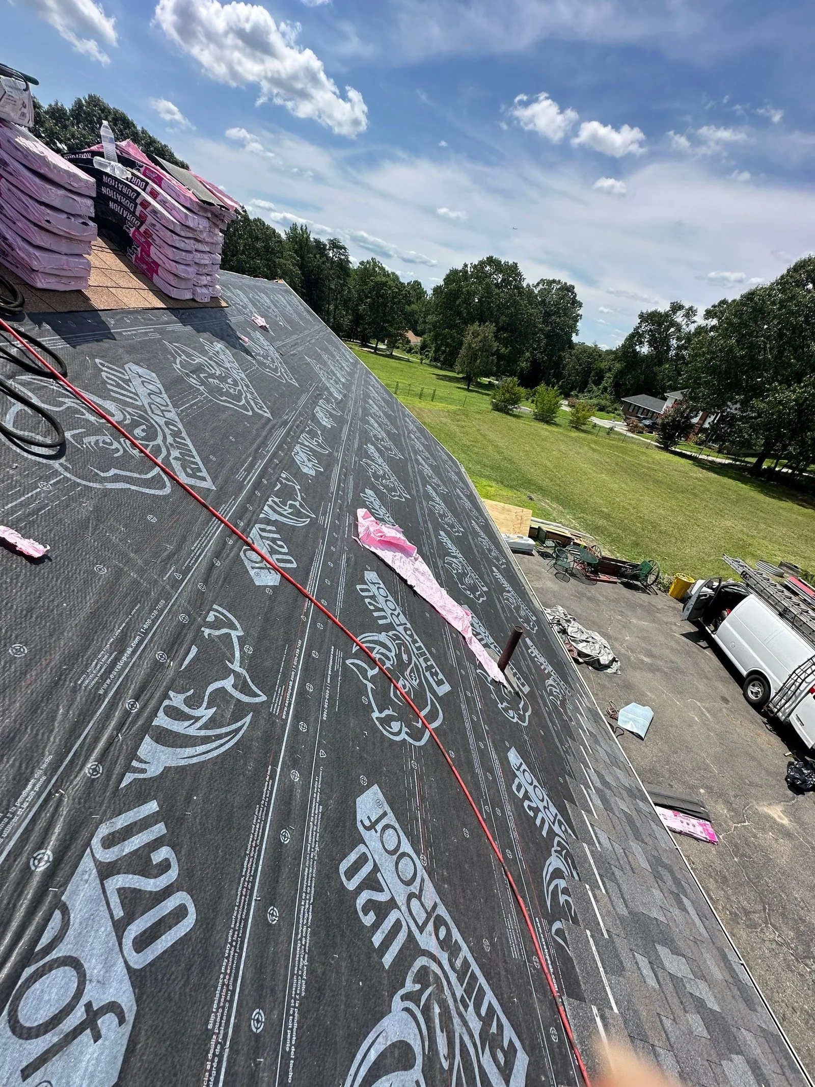 Synthetic underlayment down across the deck with shingle bundles staged at the ridge and a chalk snap line struck