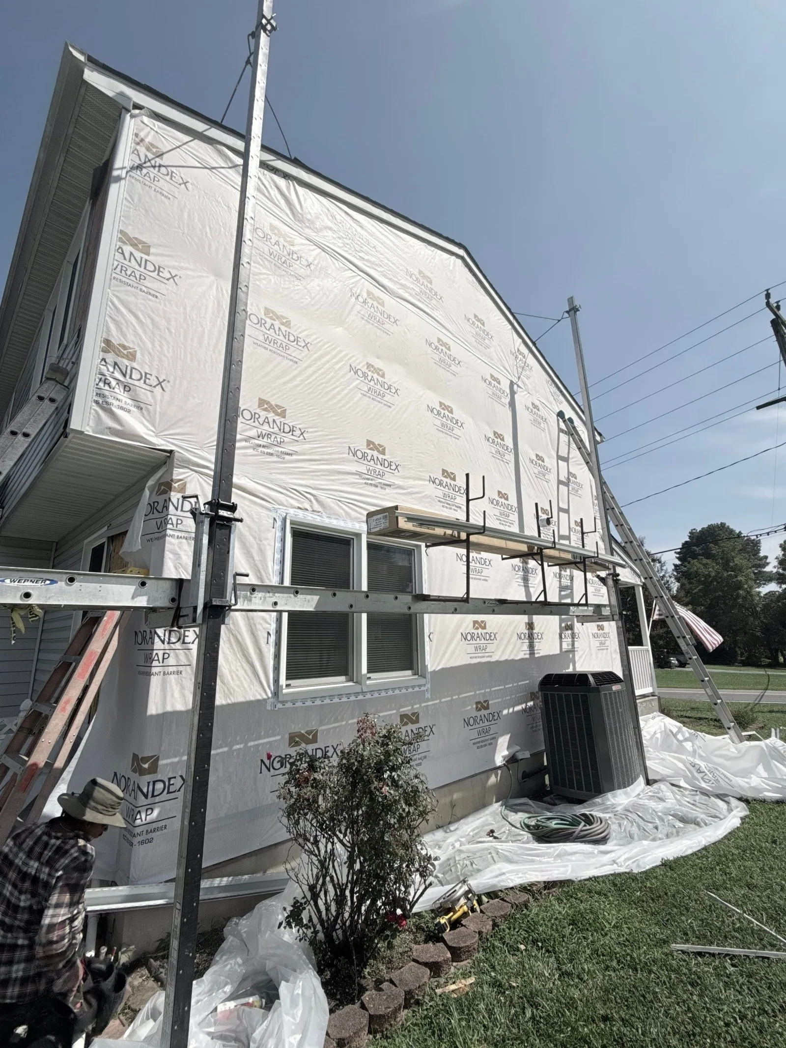 Two-storey elevation covered in Norandex weather-resistant barrier with pump-jack staging across the wall