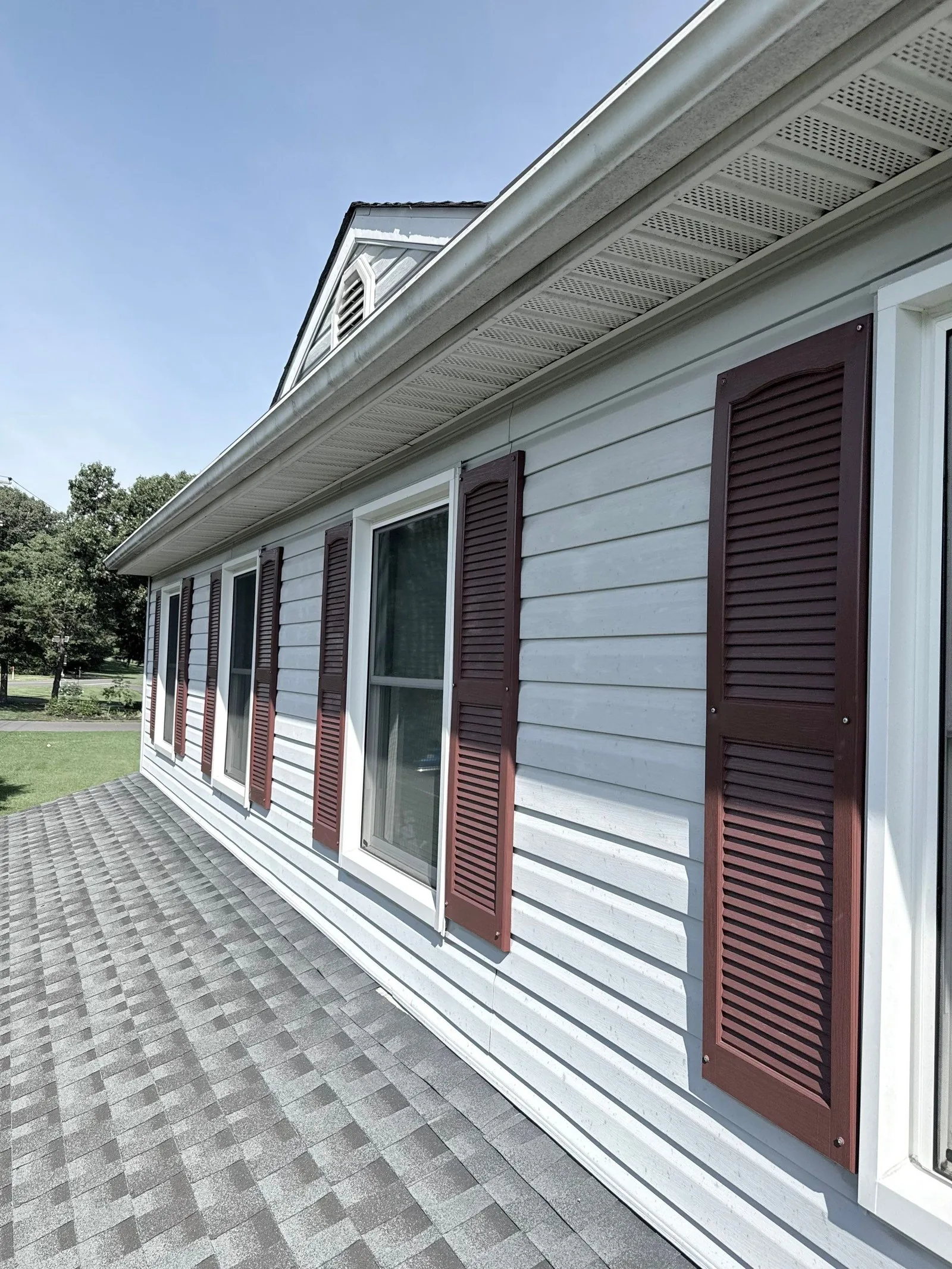 Long wall in its original light-gray lap siding with burgundy shutters, viewed from the lower shingle roof