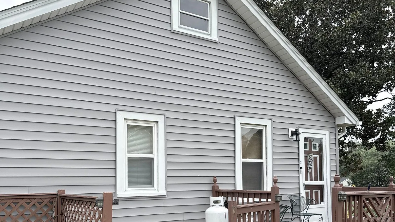 Rear corner of the house finished in new gray siding, with the wood deck, steps and concrete patio