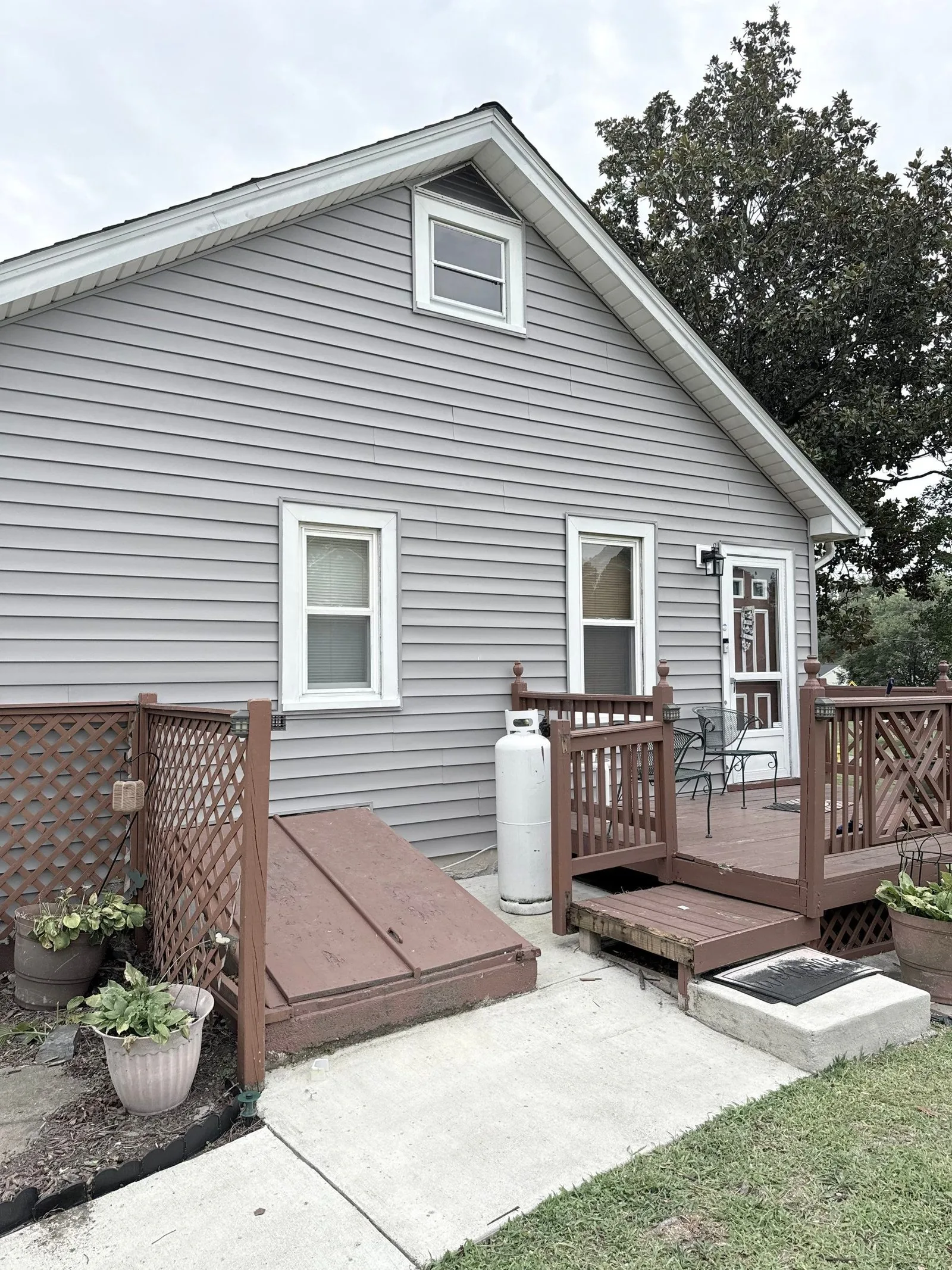 Rear corner of the house finished in new gray siding, with the wood deck, steps and concrete patio