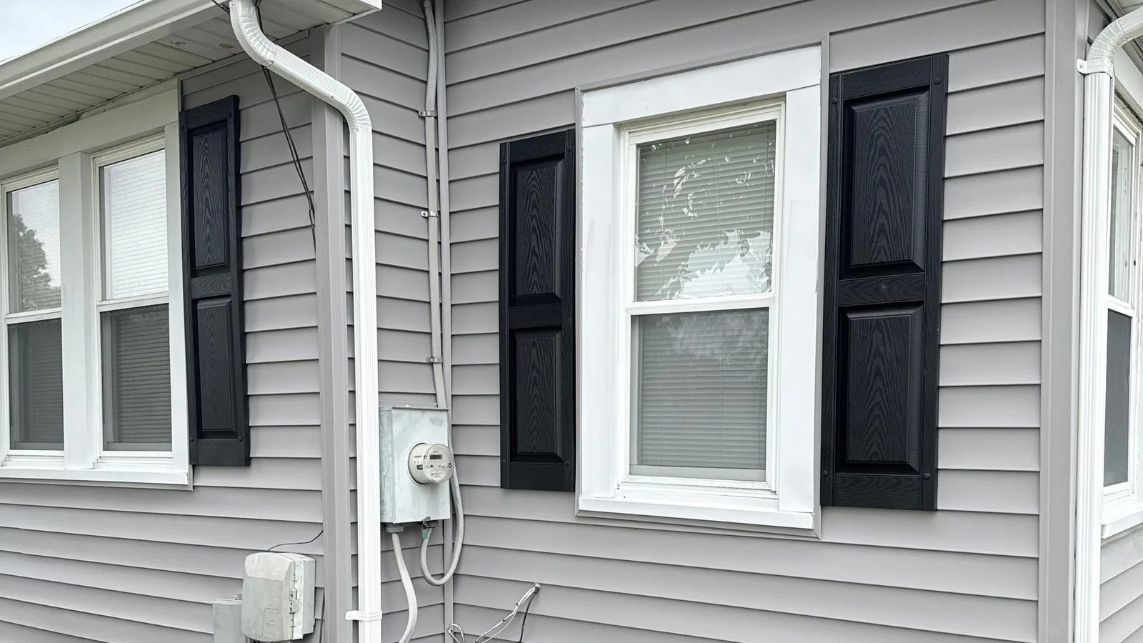 Side elevation in new gray siding with black shutters, downspout and mulch bed