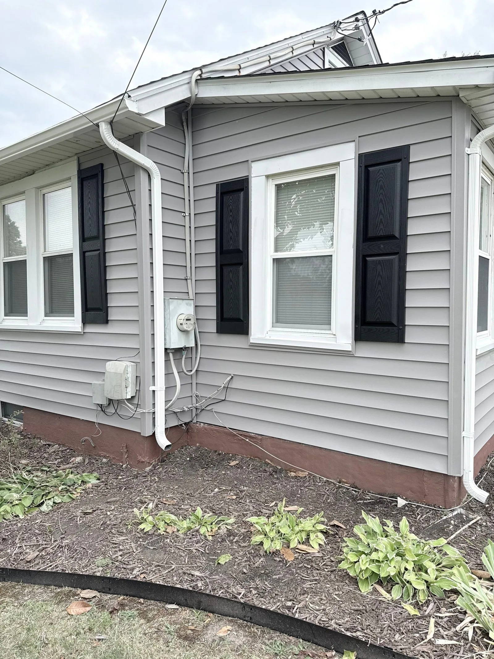 Side elevation in new gray siding with black shutters, downspout and mulch bed