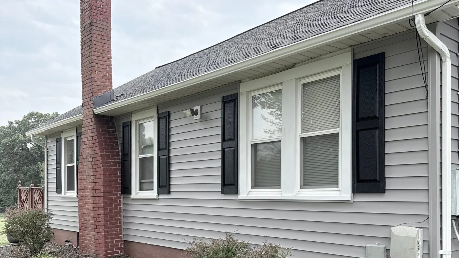 Side elevation in new gray siding with black shutters beside the red brick chimney