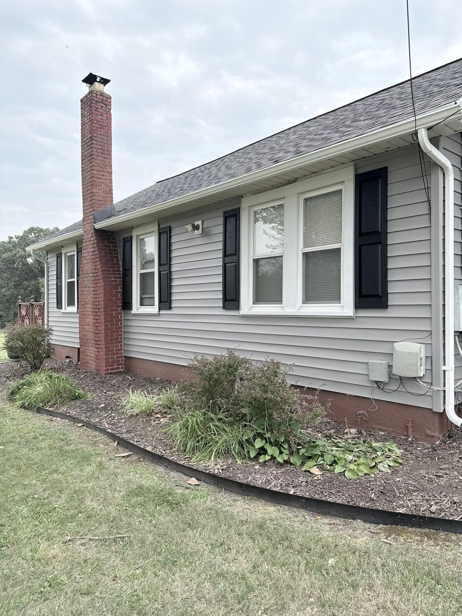 Side elevation in new gray siding with black shutters beside the red brick chimney