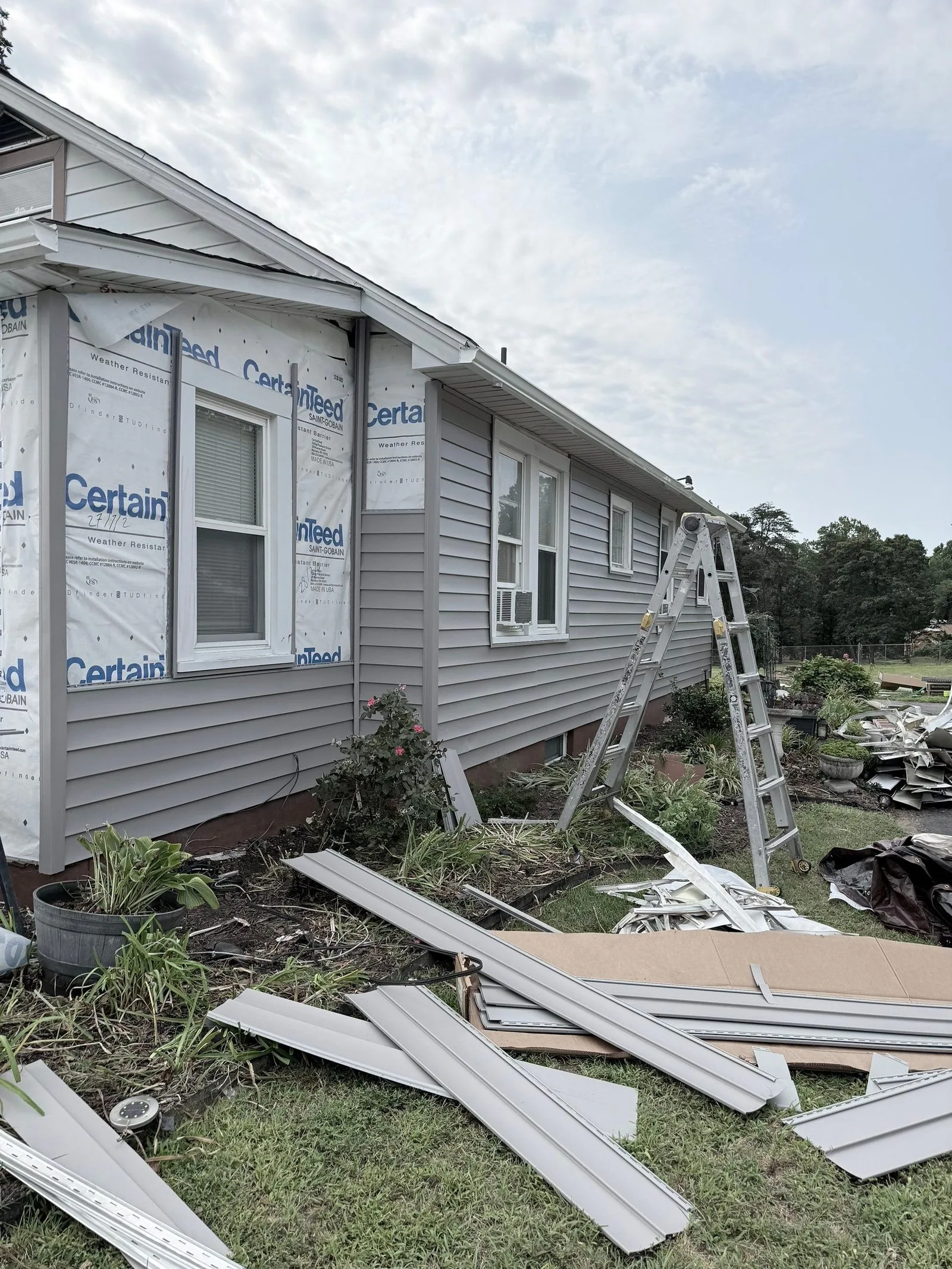House wall stripped to the house wrap with a ladder to the eave and the old siding on the lawn