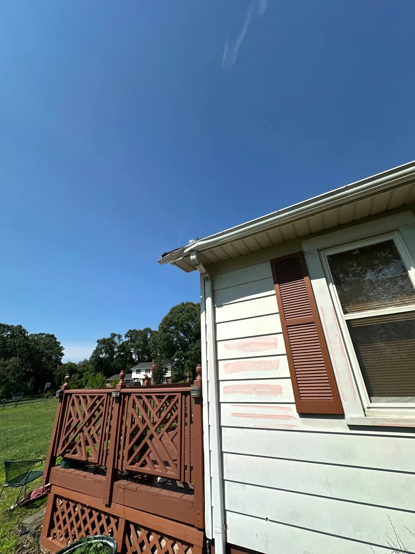 Rear corner of the house in its original white siding with brown shutters, pink chalk inspection marks on the wall