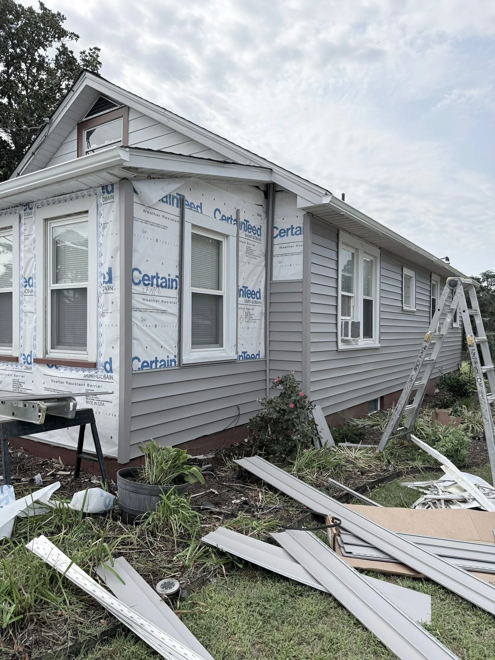 Siding stripped off down to the house wrap, torn panels scattered across the grass