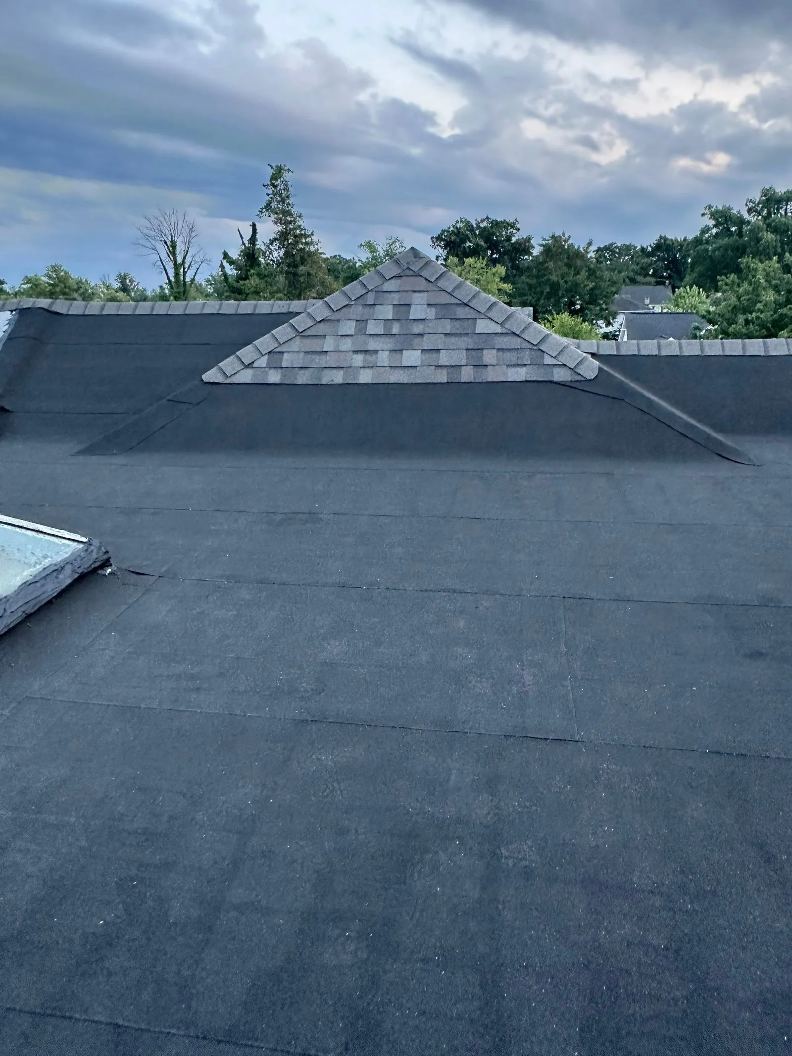 Finished low-slope roof in smooth black modified bitumen, with a shingled gable dormer and shingled caps on the parapet