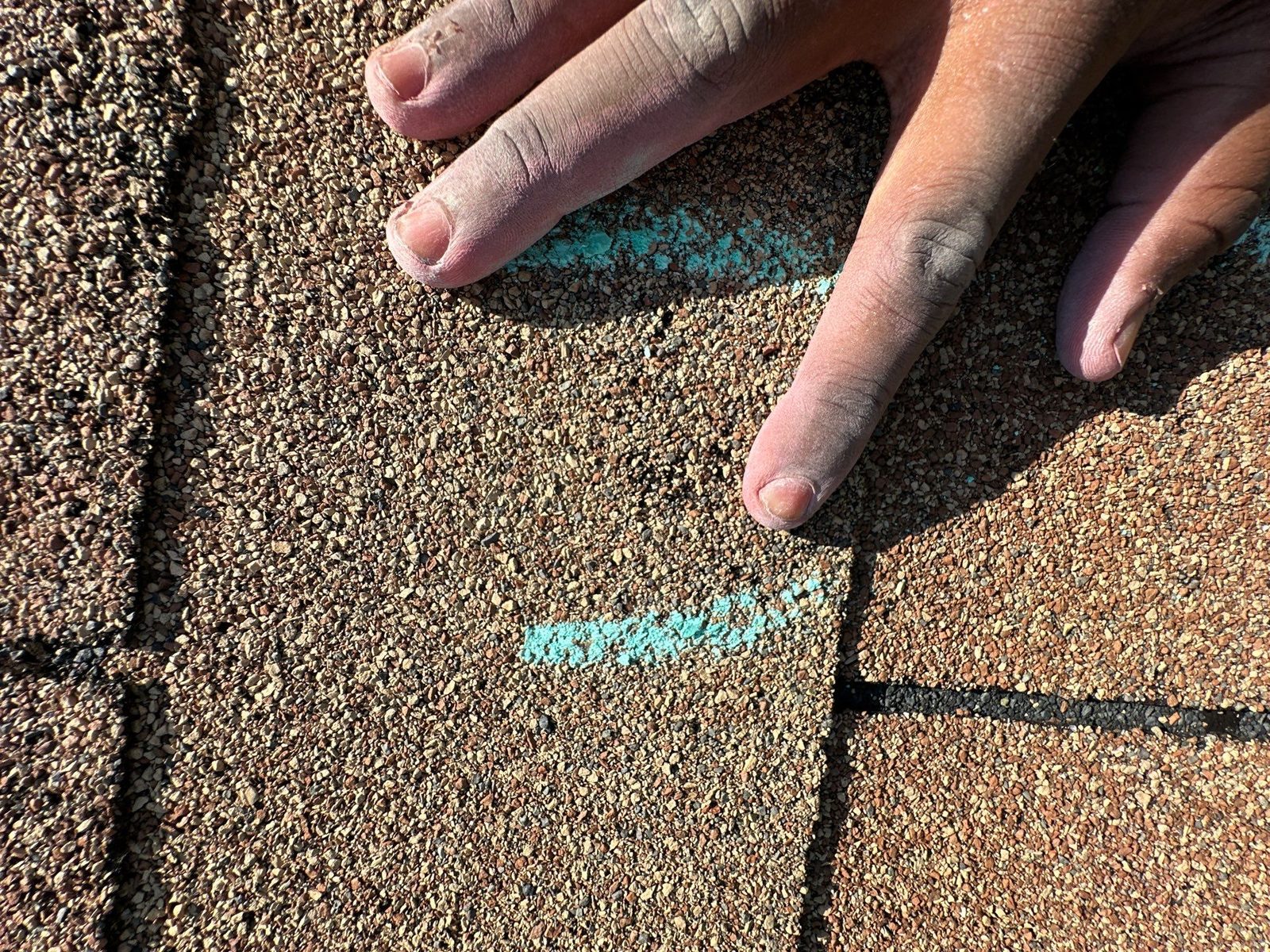 A single chalk mark on a three-tab shingle surface with a hand beside it for scale